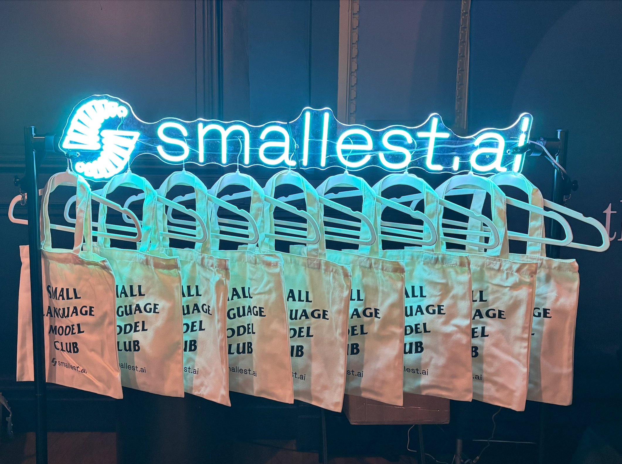 Smallest AI neon sign with Small Language Model Club tote bags hanging below
